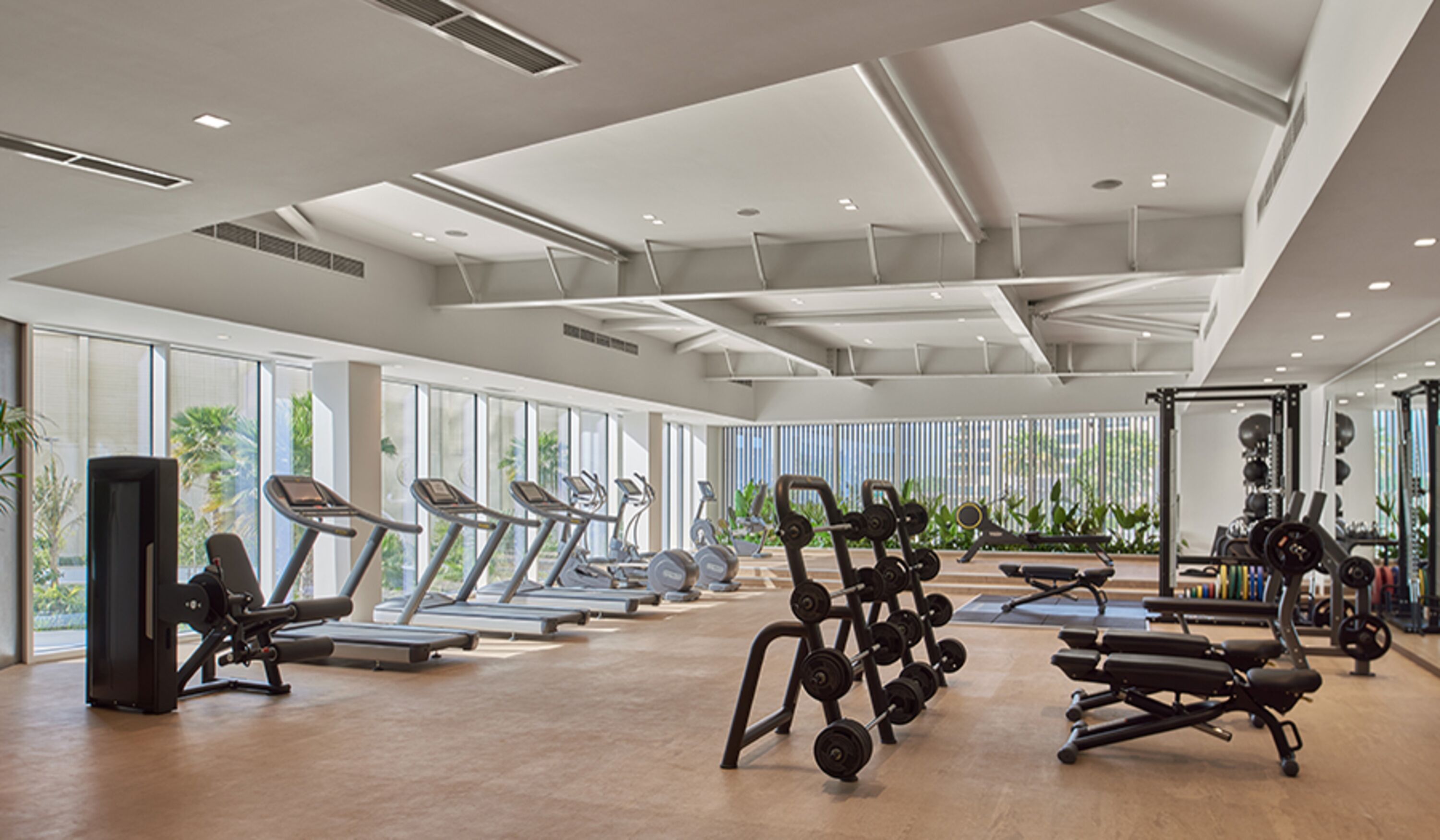 Une salle de sport moderne équipée de tapis de course, d’appareils de musculation et d’une grande fenêtre donnant sur un paysage verdoyant.