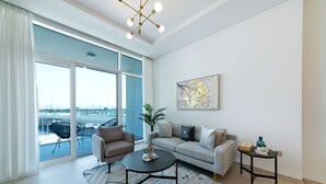 Un soggiorno moderno con divano, poltrona, tavolino da caffè e vista sulla città attraverso ampie finestre.