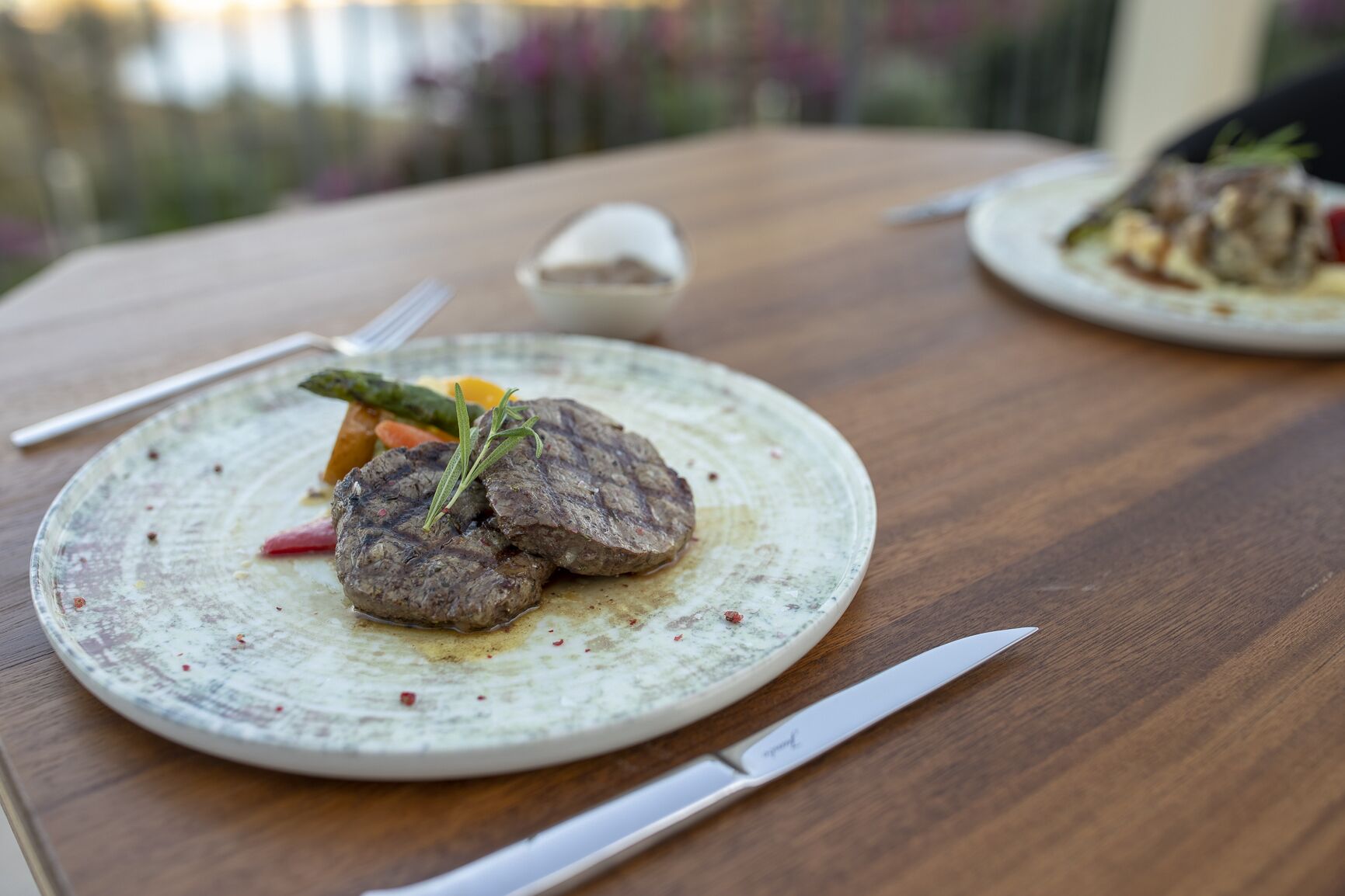 Una mesa de madera con un plato de comida, un cuchillo y un tazón pequeño.