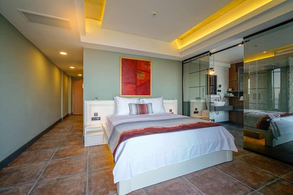 Una habitación de hotel moderna con una cama grande, una cabina de ducha de vidrio y vistas a la ciudad.