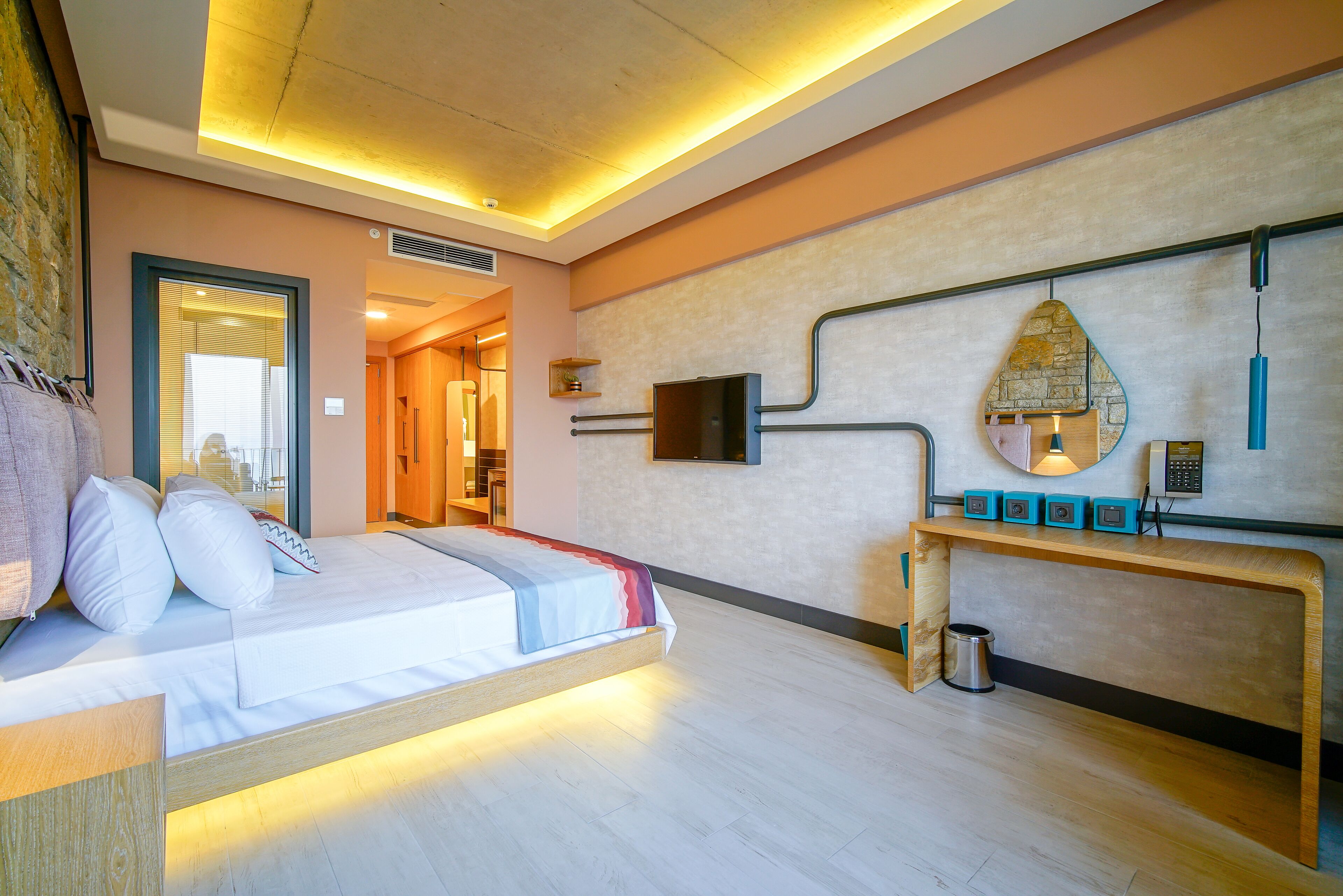 A hotel room with a bed, bedside table, wall-mounted TV, and a small console table with a phone and speakers.