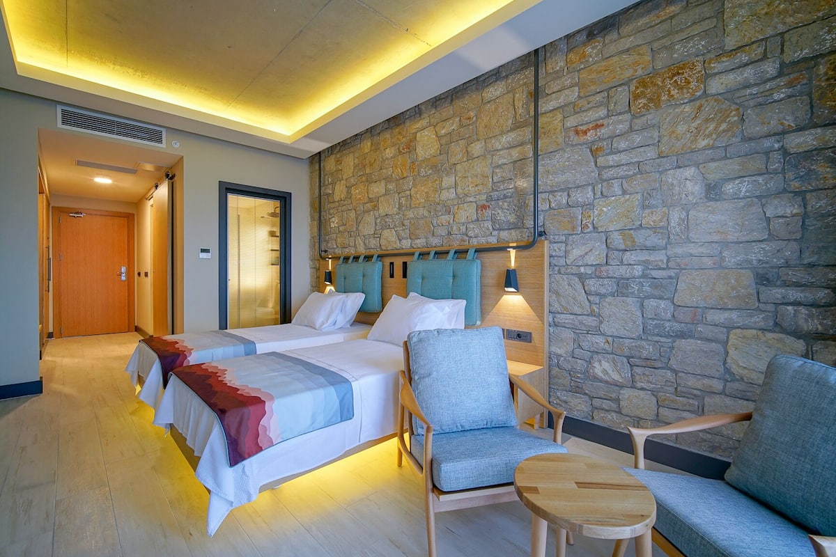Habitación de hotel con dos camas, una pared de piedra, una puerta de madera y una zona de estar con una mesa.
