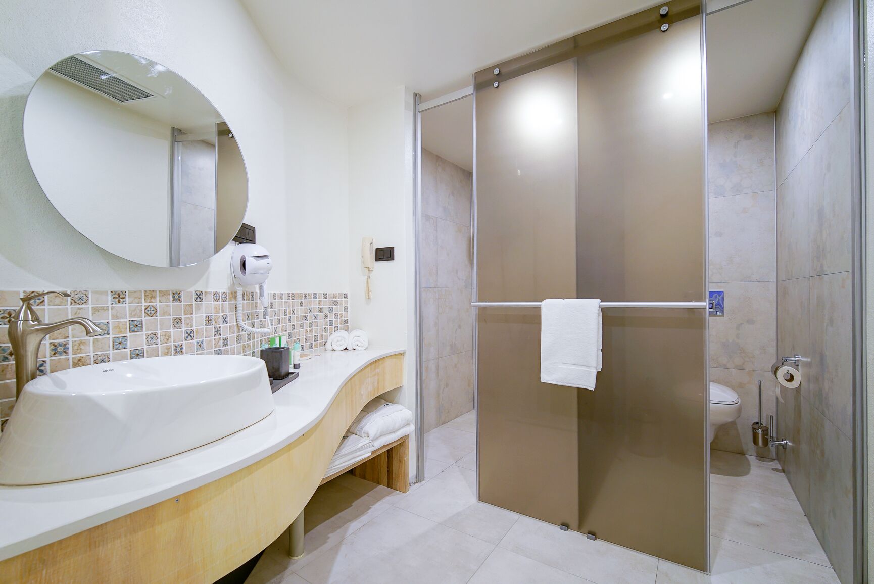 A modern bathroom with a large sink, a mirror, a hairdryer, and a shower enclosure.