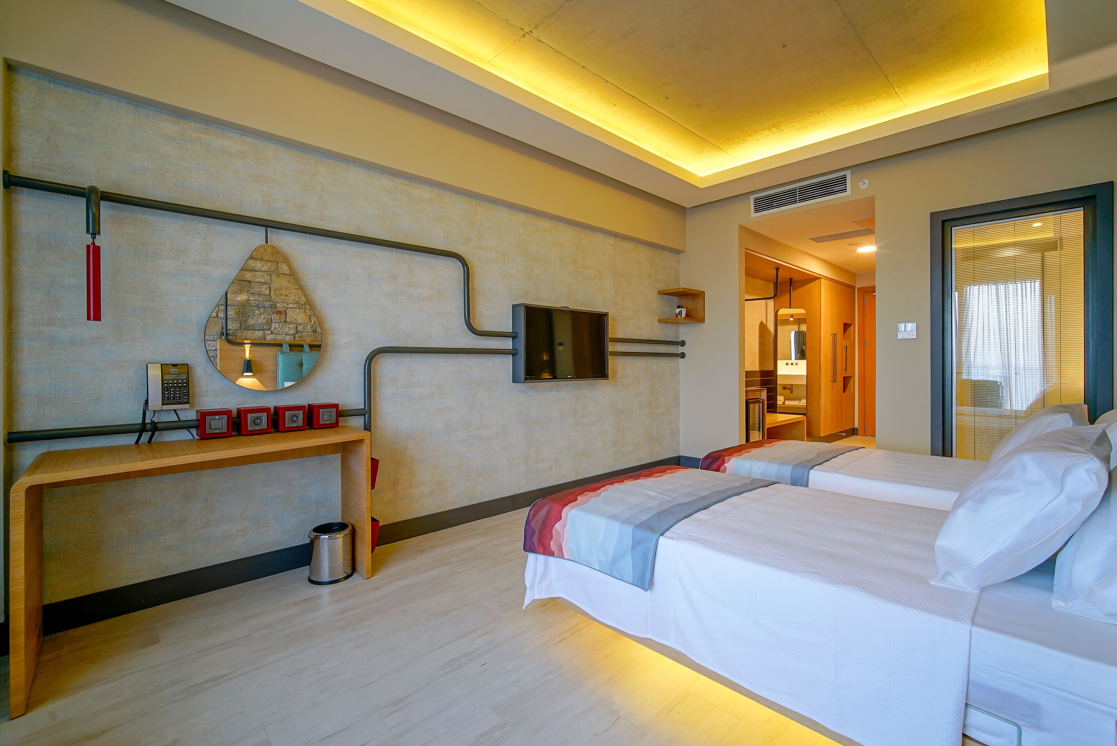 Ein Hotelzimmer mit zwei Betten, einem Holzkonsolentisch, einem Spiegel, einem Fernseher und einer kleinen Mülltonne.