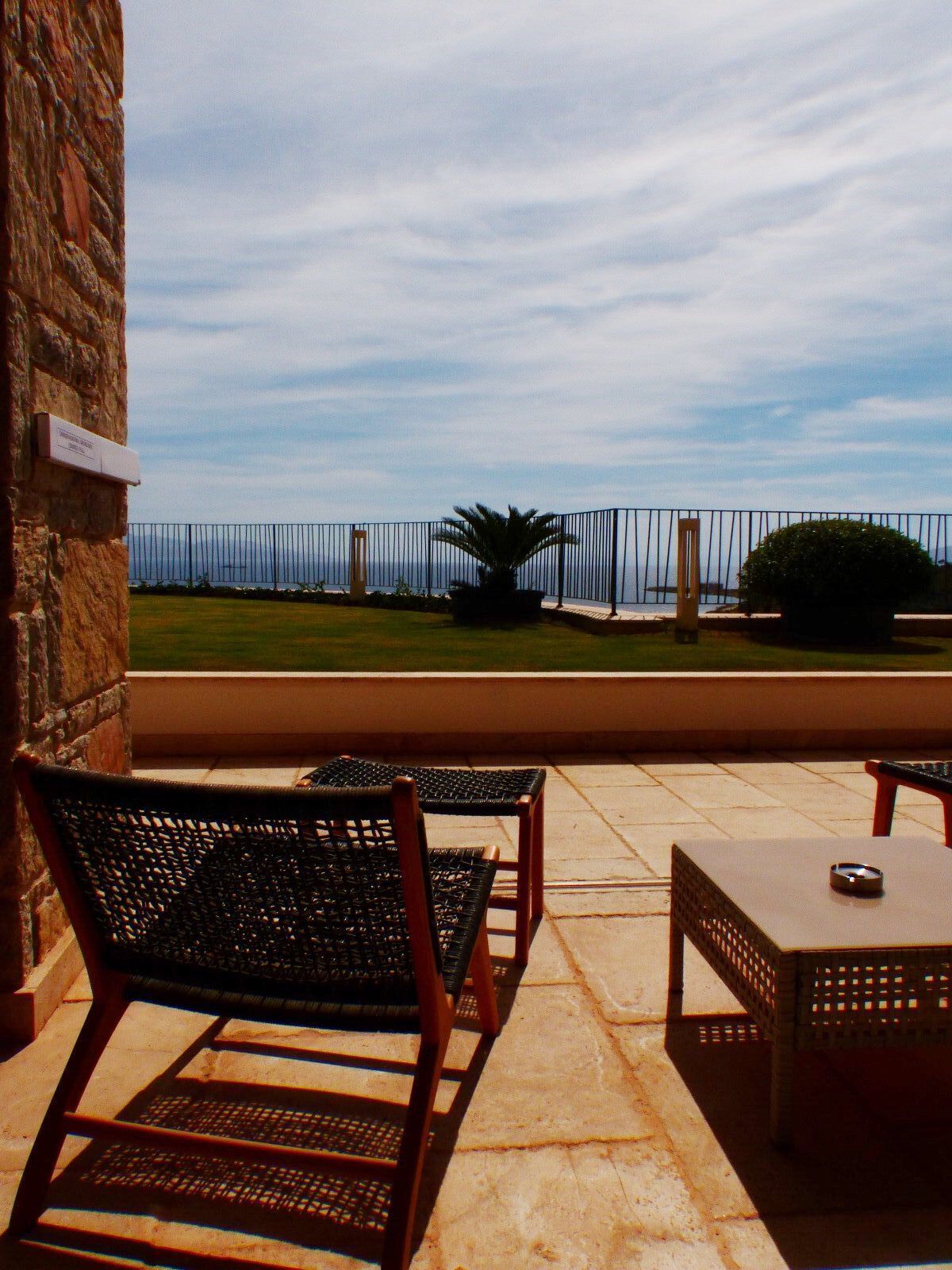 A patio area with two wicker chairs and a small table, overlooking a grassy area and a body of water.