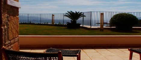 A patio area with two wicker chairs and a small table, overlooking a grassy area and a body of water.