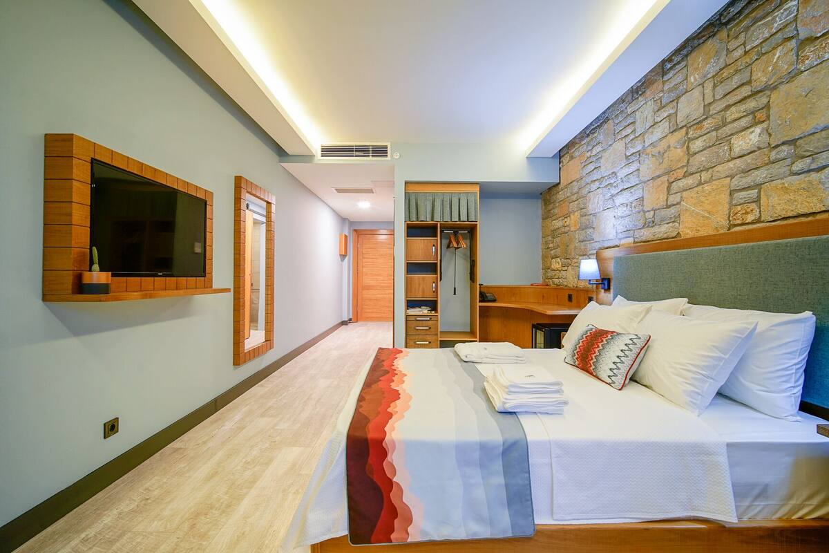 Una habitación de hotel con cama, televisión, armario y pared de piedra.