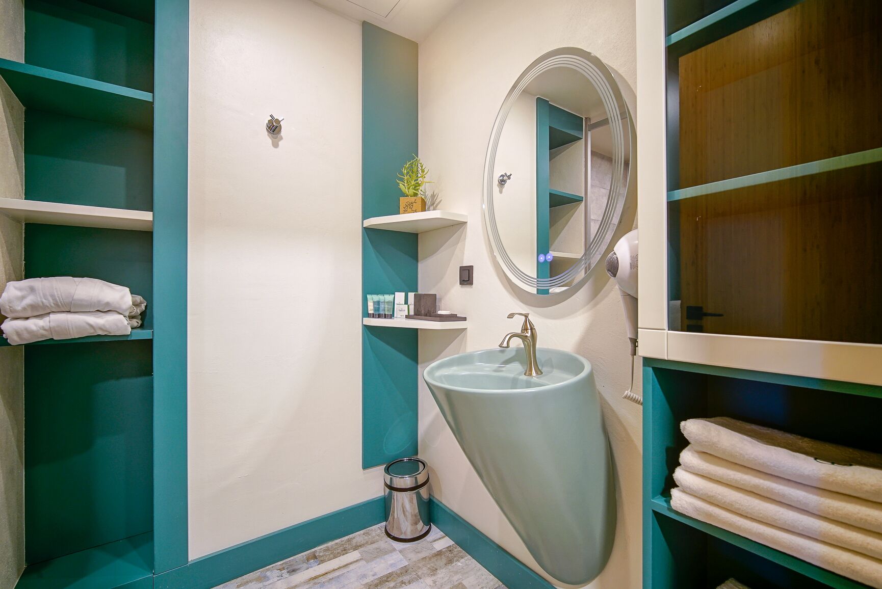 Un bagno con pareti verde acqua e bianche, un lavandino con uno specchio, mensole con asciugamani e un cestino.