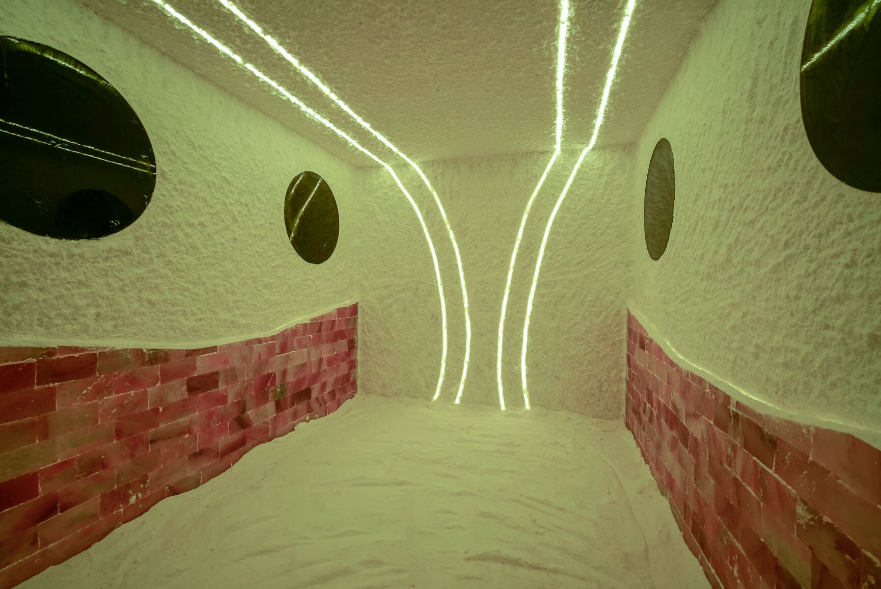 A room with a brick wall, a circular window, and a ceiling with light strips.