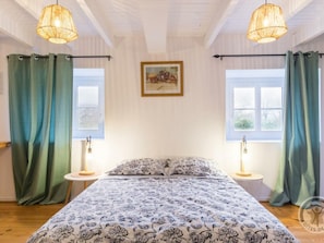 Un dormitorio con cama, dos mesitas de noche, una ventana con cortinas y un cuadro en la pared.