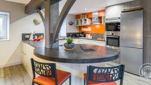 A modern kitchen with a central island, built-in appliances, and a unique ceiling structure. - Charming house 1km from Sciotot beach (Les Pieux)