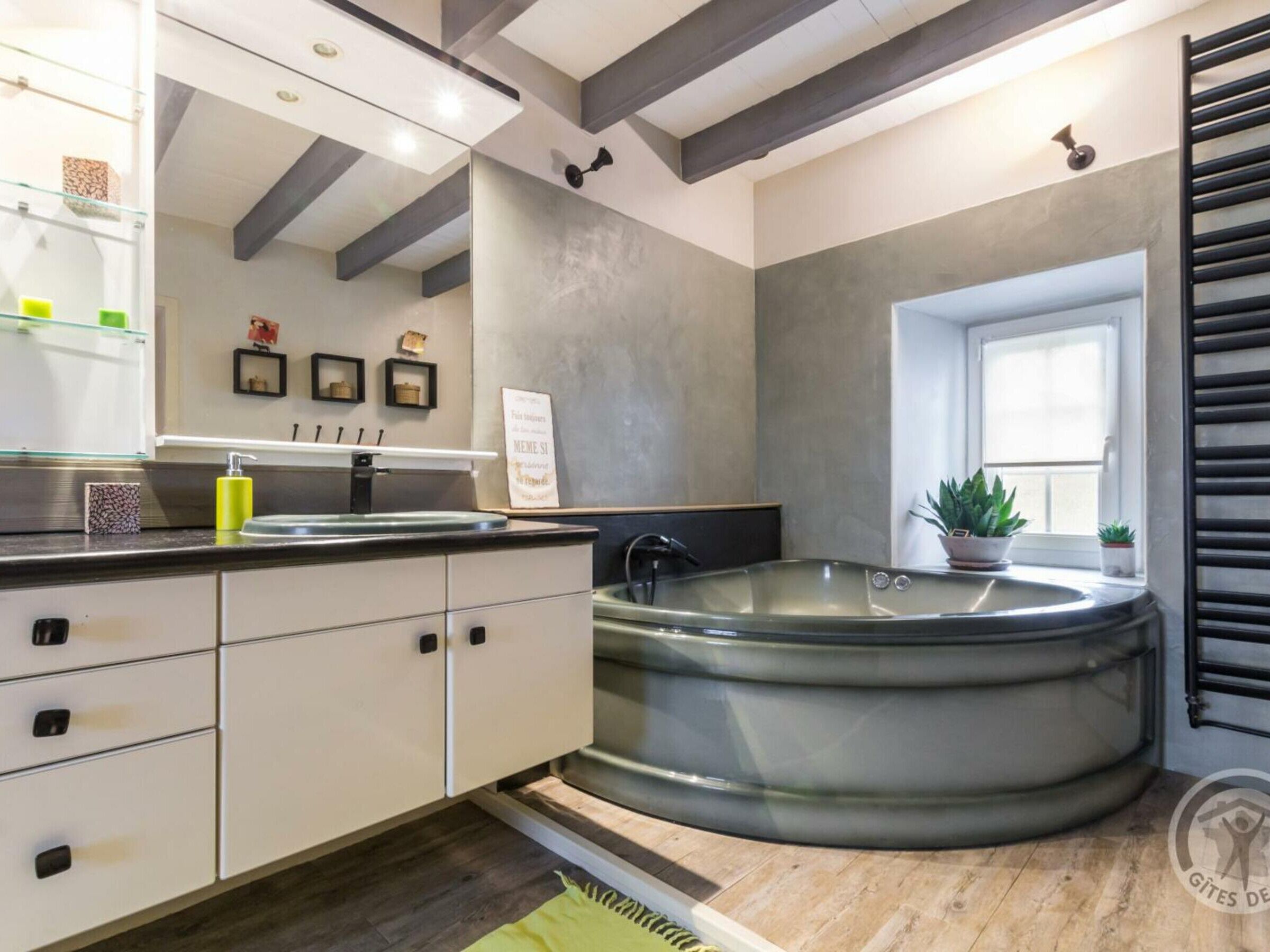 A modern bathroom with a large bathtub, a vanity with a mirror, and a window.