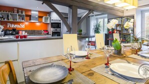 A modern kitchen with a visible 'Polvere&Sel' sign, a dining area with a wooden table set for two, and a view of the kitchen through an open door. - Charming house 1km from Sciotot beach (Les Pieux)