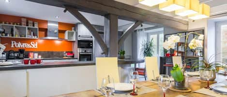 A modern kitchen with a visible 'Polvere&Sel' sign, a dining area with a wooden table set for two, and a view of the kitchen through an open door.