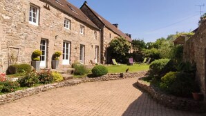 A stone building with a paved courtyard, a lawn, and two lounge chairs. - Charming house 1km from Sciotot beach (Les Pieux)
