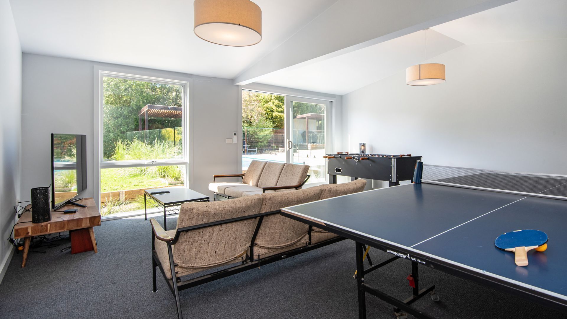 A modern room with a ping pong table, a sofa, and a TV.