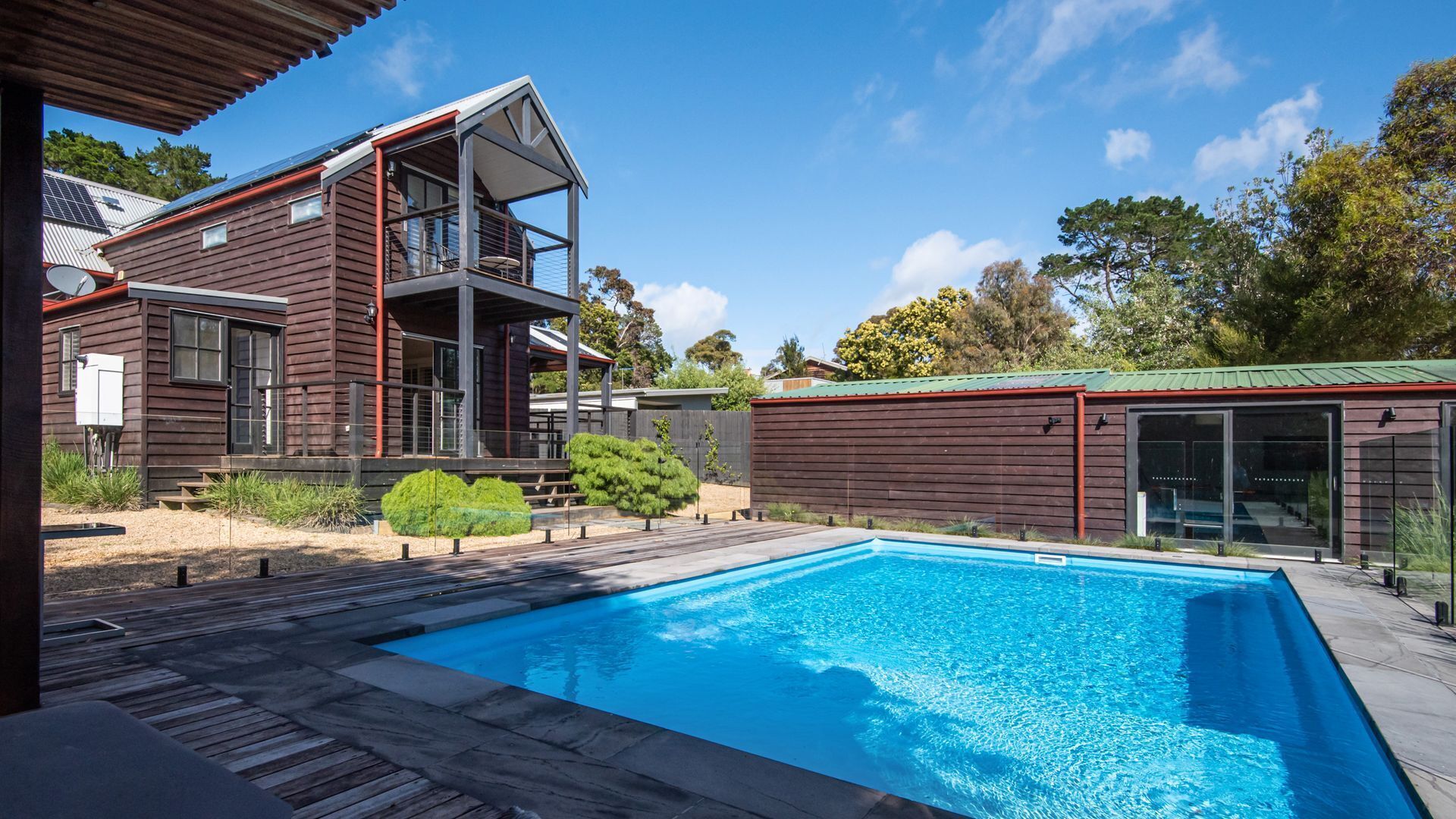 A modern house with a swimming pool, wooden deck, and a covered outdoor area.