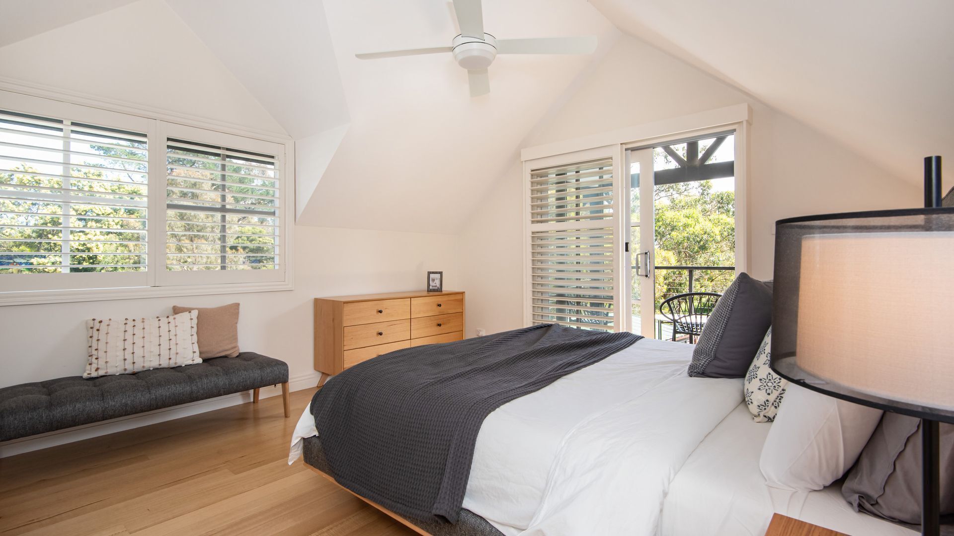 Une chambre à coucher comprenant un lit, une table de chevet, une commode et une fenêtre avec des stores.