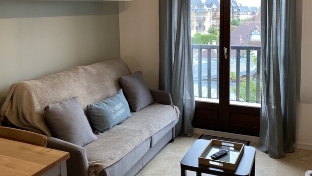 Ein Wohnzimmer mit einer Couch, einem Couchtisch, einem Schrank und Blick auf einen Balkon mit Vorhängen.