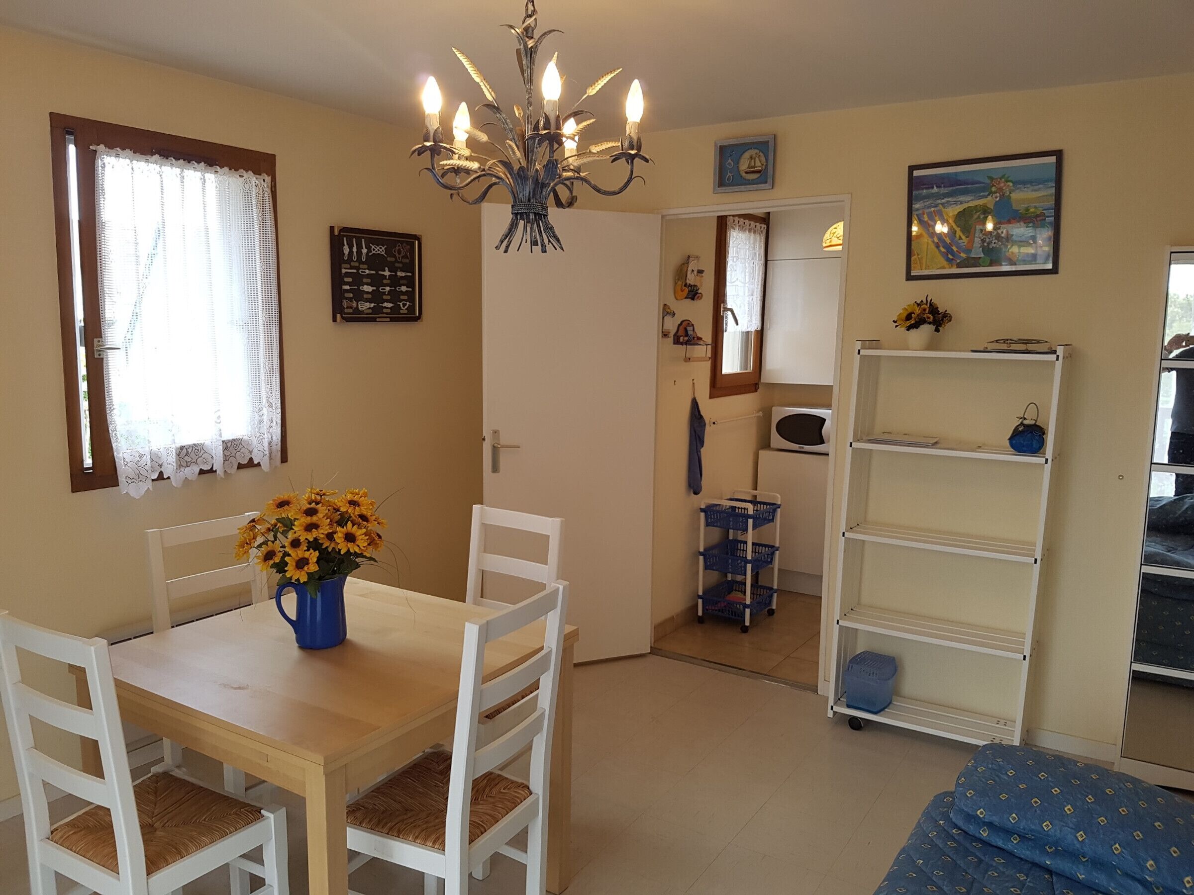 Une pièce comprenant une table à manger, des chaises, un lustre, un lit, une étagère et une porte donnant sur une autre pièce.