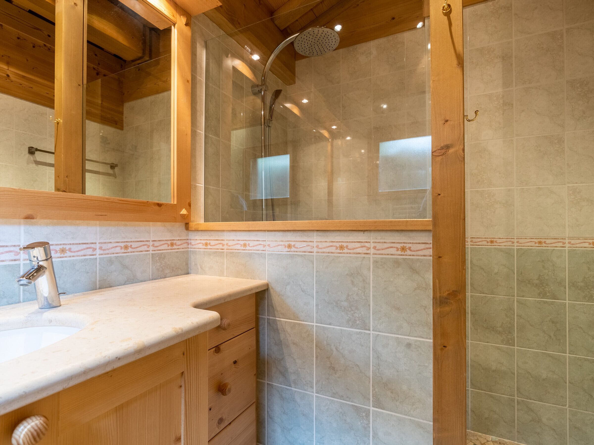 A bathroom with a wooden vanity, a glass shower enclosure, and tiled walls.