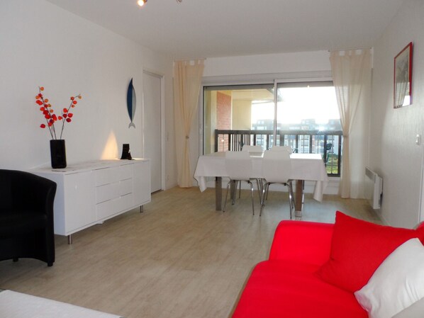 A modern living room with a red sofa, a white dining table, and a balcony with a view.