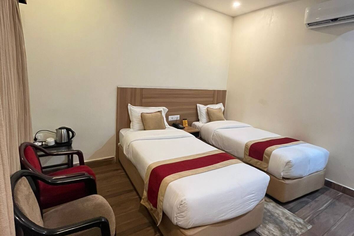 Ein Hotelzimmer mit zwei Einzelbetten, einem kleinen Schreibtisch mit Stuhl und einer Klimaanlage an der Wand.