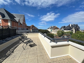 A rooftop terrace with a railing, a few lounge chairs, and a view of residential buildings.