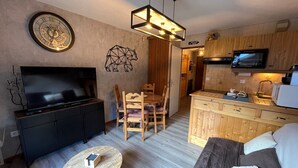 Un espace de vie compact comprenant un téléviseur, des meubles en bois, une table à manger et un coin cuisine.