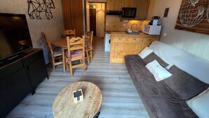 Un espace de vie compact comprenant un canapé, une table à manger, des chaises, un téléviseur, un coin cuisine avec un four à micro-ondes et une petite table ronde.
