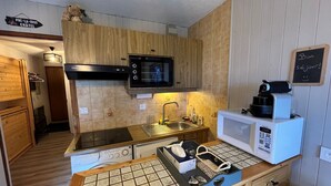 Une cuisine compacte avec des meubles en bois, un four à micro-ondes, une machine à café et un dosseret carrelé.