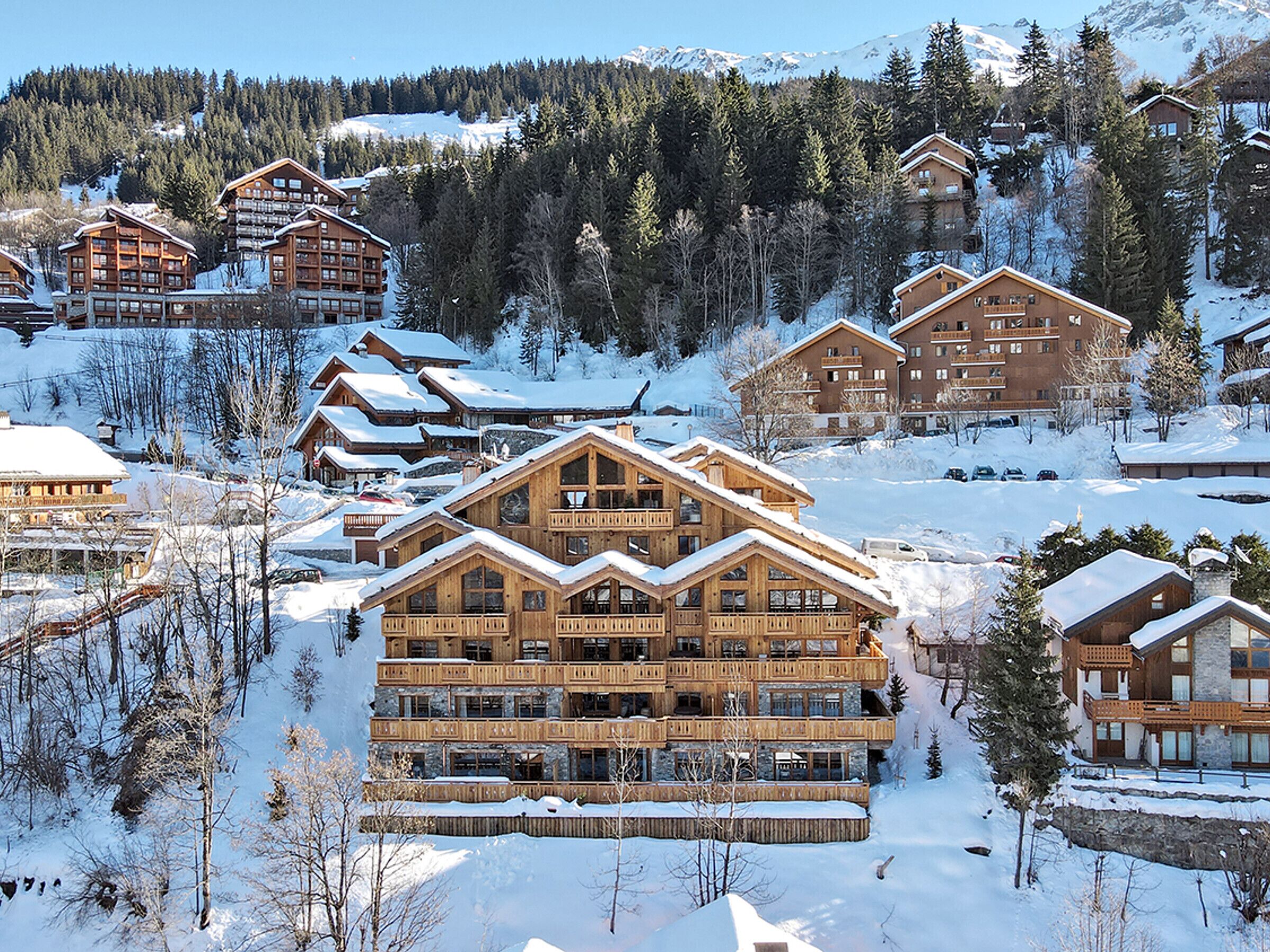 A snow-covered lodge with multiple floors and balconies, surrounded by trees and a mountainous backdrop.