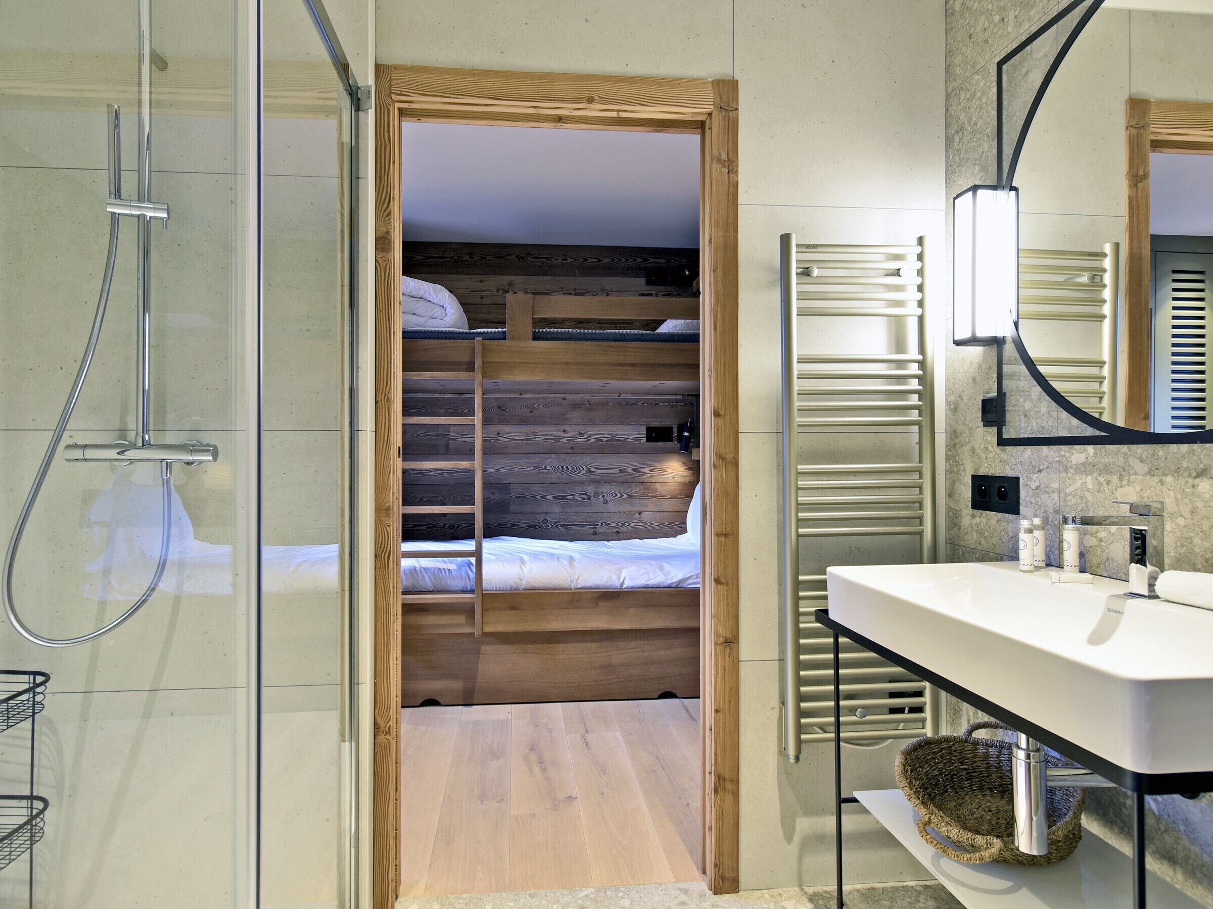Een moderne badkamer met een douche, een houten stapelbed en een witte wastafel met spiegel.