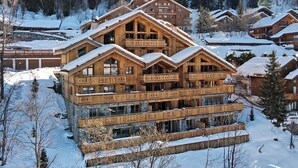 A multi-story wooden lodge with balconies, surrounded by snow-covered trees and other lodges. - Charming Apartment in Méribel - 3 Bedrooms, 6 Pers, Balcony & TV, Services Included (Méribel)