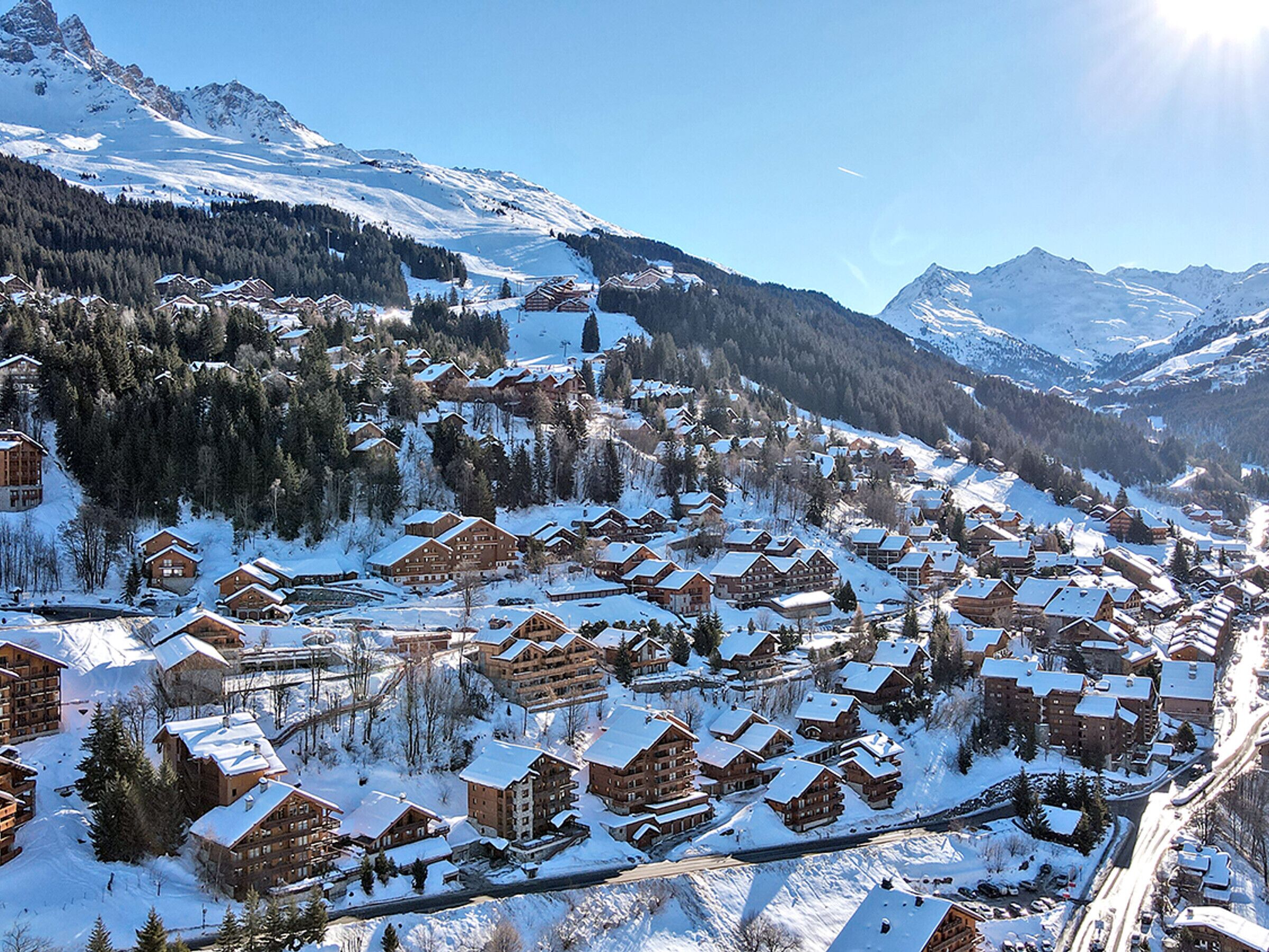 A snow-covered mountain village with wooden buildings, a ski slope, and a clear sky.