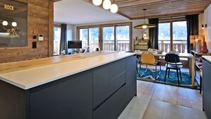 A modern kitchen with a large island, wooden ceiling, and large windows offering a view of the outdoors. - Charming Apartment in Méribel - 3 Bedrooms, 6 Pers, Balcony & TV, Services Included (Méribel)