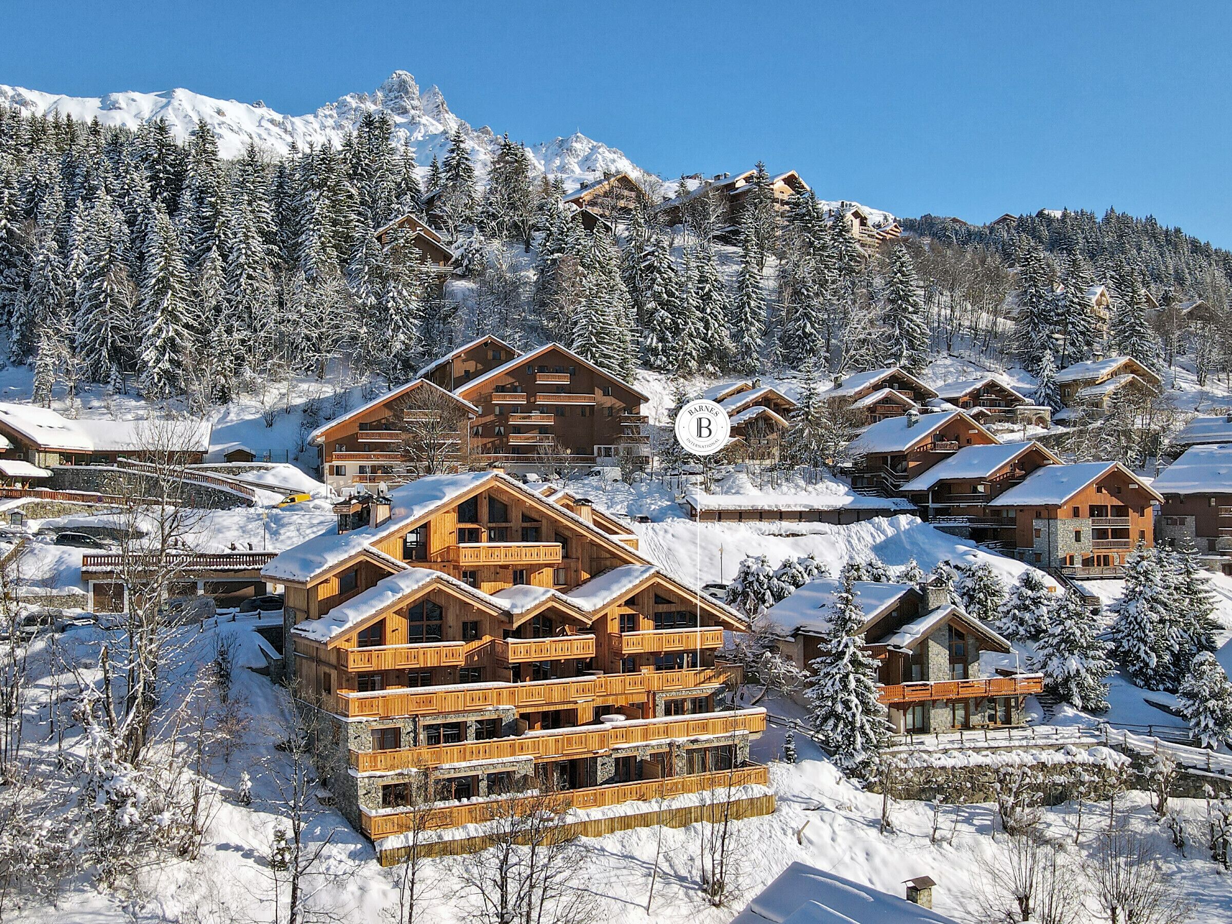 A snow-covered mountain resort with wooden chalets, a ski lift, and a clear blue sky.