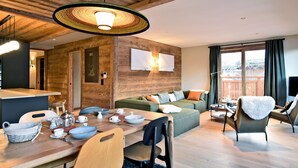 A modern living room with a wooden ceiling, a dining table set with dishes, a sofa, and a chair. - Charming Apartment in Méribel - 3 Bedrooms, 6 Pers, Balcony & TV, Services Included (Méribel)