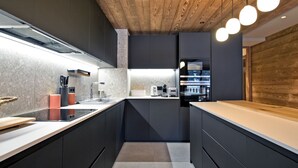 A modern kitchen with dark cabinetry, a wooden ceiling, and pendant lighting. - Charming Apartment in Méribel - 3 Bedrooms, 6 Pers, Balcony & TV, Services Included (Méribel)