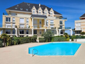 A swimming pool with a metal ladder, surrounded by a paved area with a hedge.