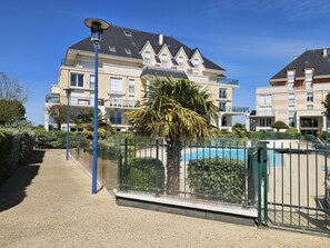 A residential building with a pool, surrounded by greenery and a clear sky.