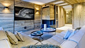 Un salon moderne doté d’un grand téléviseur à écran plat fixé sur un mur en bois, d’un ensemble de canapés, d’une table basse et d’un mur décoratif en pierre.