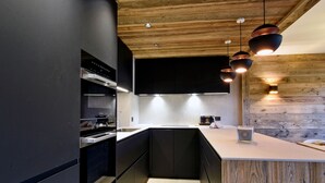 Une cuisine moderne avec des meubles de couleur sombre, un plafond en bois et des luminaires suspendus.