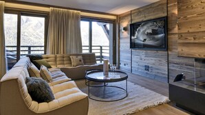 Un salon moderne avec un canapé d’angle, une table basse ronde et un téléviseur fixé à un mur en bois.