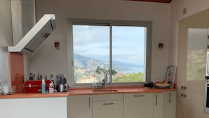 Una cocina moderna con un amplio ventanal, armarios blancos y techo de madera.