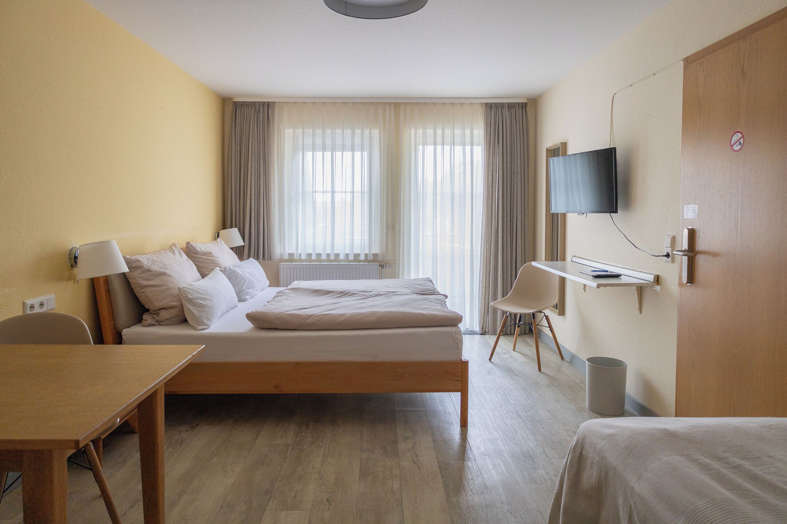 A hotel room with a bed, bedside tables, a TV, a desk, and a chair.