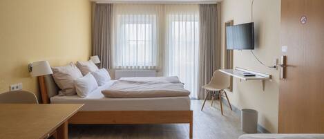 A hotel room with a bed, bedside tables, a TV, a desk, and a chair.