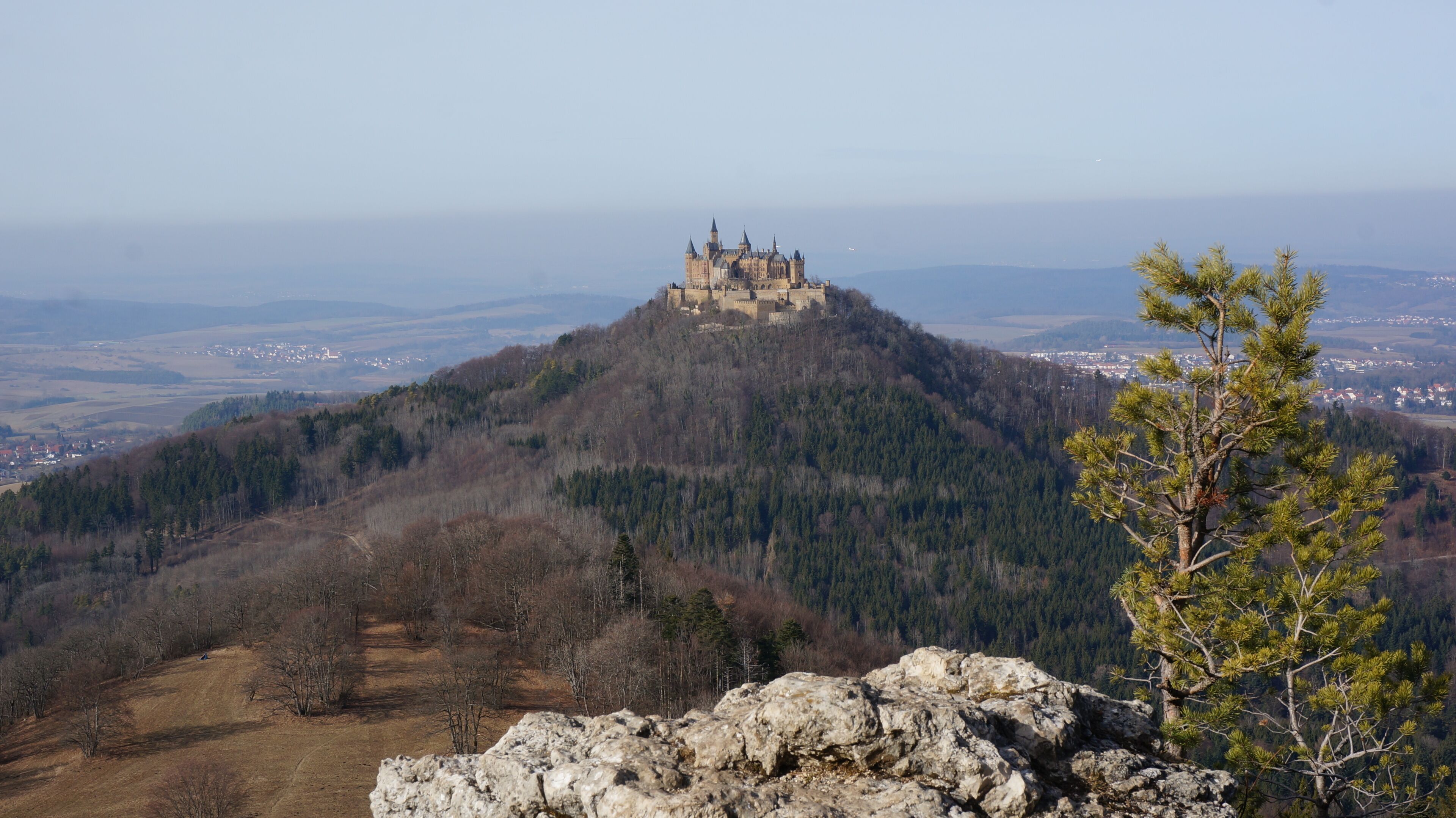 Un château perché sur une colline, entouré d’un paysage boisé et offrant une vue dégagée sur les environs.