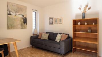 A living room with a grey sofa, a wooden table, a bookshelf, and a large abstract painting.