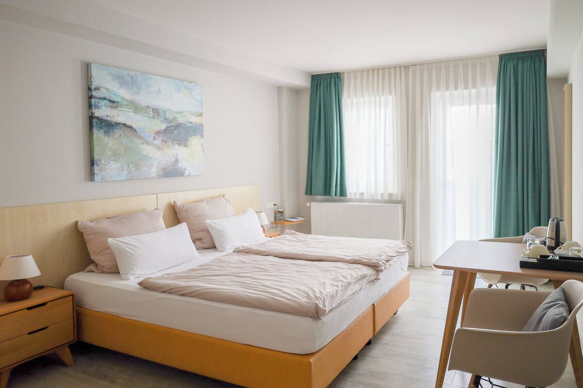 A hotel room with a bed, bedside table, lamp, and a painting on the wall.